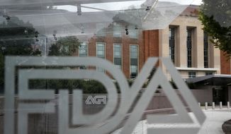 The U.S. Food and Drug Administration building behind FDA logos at a bus stop on the agency&#x27;s campus in Silver Spring, Md., on Aug. 2, 2018. The FDA has approved the first combination test for flu and COVID-19 that can be used at home, giving consumers an easy way to determine if a runny nose is caused by either disease. (AP Photo/Jacquelyn Martin, File)