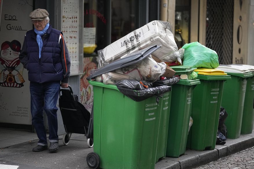 A man walks past not collected garbage cans, Thursday, March 9, 2023 in Paris. The show of anger against President Emmanuel Macron&#x27;s plan to raise the retirement age from 62 to 64 is set to continue in coming days, as train and metro drivers, refinery workers, garbage collectors and others have said they would continue ongoing strikes. (AP Photo/Michel Euler)