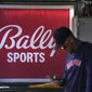 A member of the Houston Astros stands in the dugout in front of a Bally Sports sign before the team&#x27;s spring training baseball game against the St. Louis Cardinals on March 2, 2023, in Jupiter, Fla. Diamond Sports Group, the largest owner of regional sports networks, filed for Chapter 11 bankruptcy protection Tuesday, March 14. The move came after it missed a $140 million interest payment last month. Diamond owns 19 networks under the Bally Sports banner. Those networks have the rights to 42 professional teams — 14 baseball, 16 NBA and 12 NHL. (AP Photo/Jeff Roberson, File)