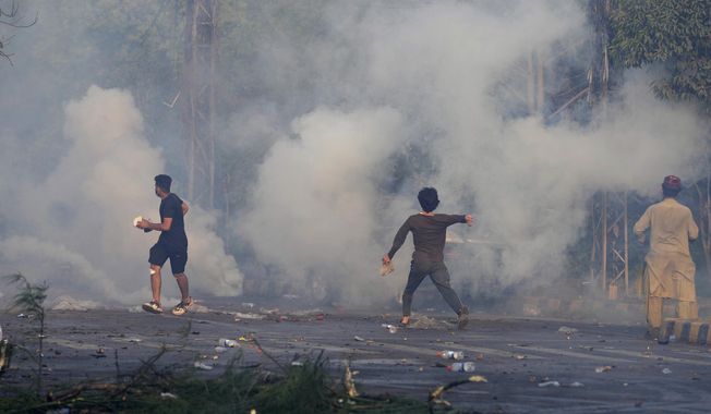 Supporters of former Prime Minister Imran Khan throw stones toward riot police officers firing tear gas to disperse them during clashes, in Lahore, Pakistan, Wednesday, March 15, 2023. Clashes between Pakistan&#x27;s police and supporters of Khan persisted outside his home in the eastern city of Lahore on Wednesday, a day after officers went to arrest him for failing to appear in court on graft charges. (AP Photo/K.M. Chaudary)