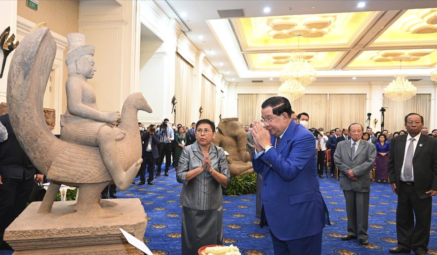 In this photo provided by Kok Ky/Cambodia&#x27;s Government Cabinet, Cambodian Prime Minister Hun Sen, center right, prays together with his minister of Culture and Fine Arts Phoeung Sackona, center left, in front of a sandstone statue at Peace Palace, in Phnom Penh, Cambodia, Friday, March 17, 2023. Centuries-old cultural artifacts that had been illegally smuggled out from Cambodia were welcomed home Friday at a celebration led by Prime Minister Hun Sen, who offered thanks for their return and appealed for further efforts to retrieve such stolen treasures. (Kok Ky/Cambodia&#x27;s Government Cabinet via AP)
