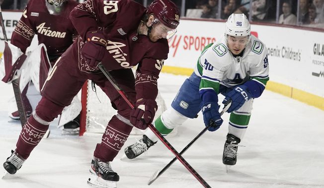 Vancouver Canucks&#x27; Andrei Kuzmenko (96) chases the puck against Arizona Coyotes&#x27; J.J. Moser (90) during the first period of an NHL hockey game Thursday, March 16, 2023, in Tempe, Ariz. (AP Photo/Darryl Webb)