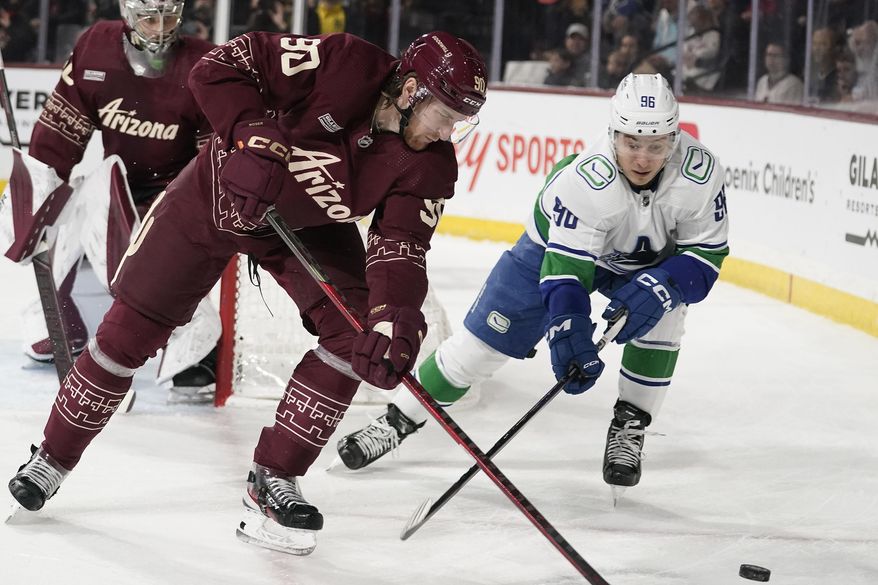 Vancouver Canucks&#x27; Andrei Kuzmenko (96) chases the puck against Arizona Coyotes&#x27; J.J. Moser (90) during the first period of an NHL hockey game Thursday, March 16, 2023, in Tempe, Ariz. (AP Photo/Darryl Webb)