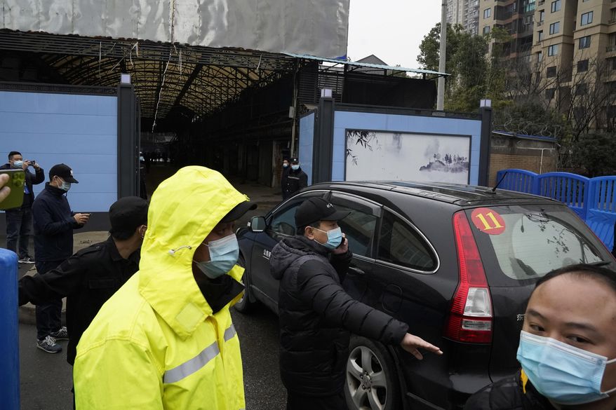FILE - In this file photo dated Sunday, Jan. 31, 2021, security personnel clear the way for a convoy of the World Health Organization team to enter the Huanan Seafood Market on the third day of field visit in Wuhan in central China&#x27;s Hubei province. International scientists have examined previously unavailable genetic data from samples collected at a market in China close to where the first human cases of COVID-19 were detected and said they have found suggestions the pandemic originated from animals, not a lab. (AP Photo/Ng Han Guan, File)