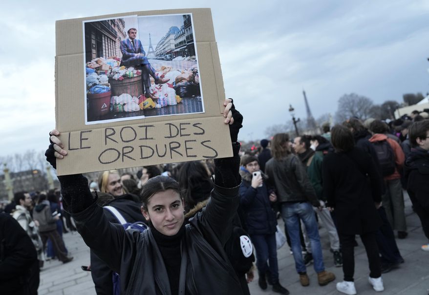 A woman holds a placard depicting French President Emmanuel Macron sitting on garbage cans that reads, &quot;king of trash&quot; during a protest in Paris, Friday, March 17, 2023. Protests against French President Emmanuel Macron&#x27;s decision to force a bill raising the retirement age from 62 to 64 through parliament without a vote disrupted traffic, garbage collection and university campuses in Paris as opponents of the change maintained their resolve to get the government to back down. (AP Photo/Lewis Joly) **FILE**