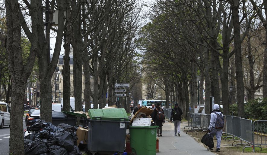 People walk past uncollected garbage in Paris, March 20, 2023 as strikes continue with uncollected garbage piling higher by the day. (AP Photo/Aurelien Morissard, File)