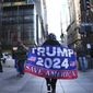 A woman walks on Fifth Avenue carrying a flag showing support for former President Donald Trump, on Tuesday, March 21, 2023, in New York. (AP Photo/Bryan Woolston)