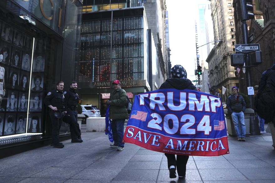 A woman walks on Fifth Avenue carrying a flag showing support for former President Donald Trump, on Tuesday, March 21, 2023, in New York. (AP Photo/Bryan Woolston)