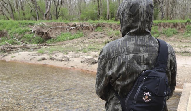 A protester stands along Intrenchment Creek in DeKalb County, Ga., near the site of a planned police training center on March 9, 2023. The protester&#x27;s button is in honor of Tortuguita, a 26-year-old activist who was fatally shot by Georgia authorities in January. (AP Photo/R.J. Rico)