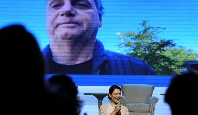 Former first lady Michelle Bolsonaro speaks at an event where she was presented as the new leader of PL Women by the Liberal Party (PL), in Brasilia, Brazil, Tuesday, March 21, 2023. Above is live video of her husband, former President Jair Bolsonaro, who attended the event virtually from Florida. (AP Photo/Eraldo Peres)