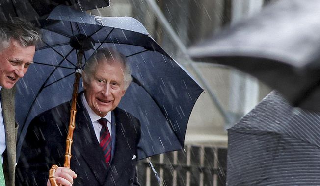 King Charles III of Great Britain, right, leaves the Brodowin ecovillage in the rain, Germany, Thursday, March 30, 2023. A heavy thunderstorm with lightning and thunder upset the strict protocol of the royal visit to the in Brandenburg. (Jens Buettner/DPA via AP, Pool)