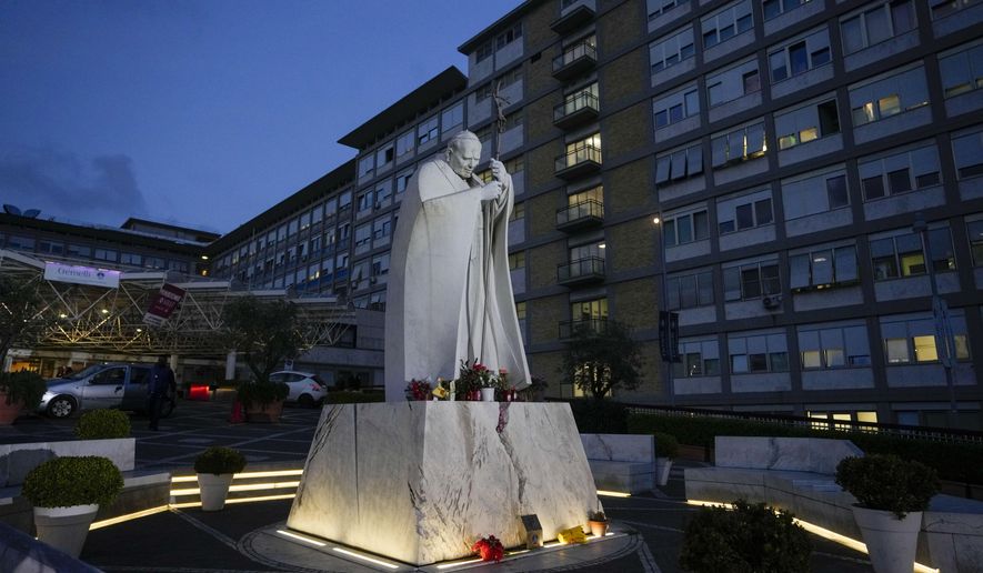 A statue of late Pope John Paul II is backdropped by the rooms on the top floor normally used when a pope is hospitalized at the Agostino Gemelli hospital, in Rome, Friday, March 31, 2023. Pope Francis is expected to be discharged on Saturday from the Rome hospital where he is being treated for bronchitis as his recovery proceeds in a 