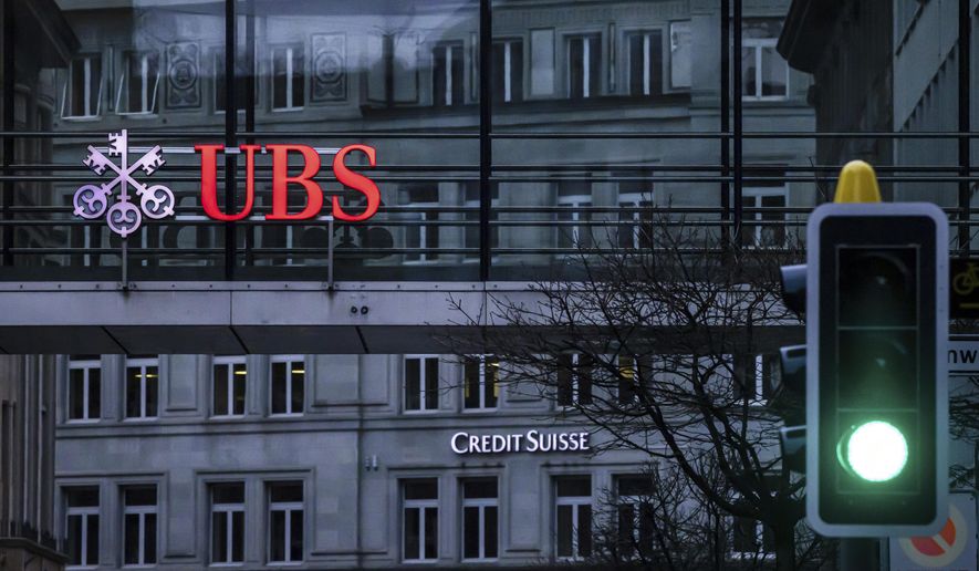 A traffic light signals green in front of the logos of the Swiss banks Credit Suisse and UBS in Zurich, Switzerland, on March 19, 2023. Analysts say the UBS takeover of embattled rival Credit Suisse has shaken Switzerland’s self-image and dented its reputation as a global financial center. They warn that the country’s prosperity could grow too dependent on a single banking behemoth. (Michael Buholzer/Keystone via AP, File)