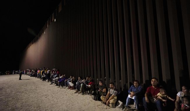 Migrants wait along a border wall Aug. 23, 2022, after crossing from Mexico near Yuma, Ariz. President Joe Biden&#x27;s administration announced in early January that it would admit up to 30,000 people a month from Cuba, Haiti, Nicaragua and Venezuela for two years with authorization to work when they apply online. Homeland Security Secretary Alejandro Mayorkas argues that the new rules are designed to weaken cartels who help migrants cross into the U.S. illegally. (AP Photo/Gregory Bull, File)