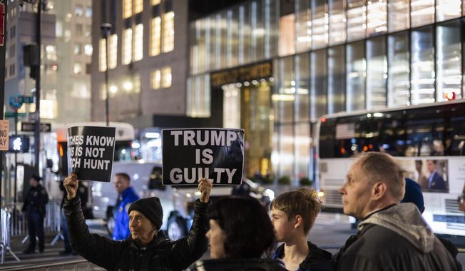 A protester holds placards outside Trump Tower in New York on Monday, April 3, 2023. Former President Donald Trump is expected to be booked and arraigned on Tuesday on charges arising from hush money payments during his 2016 campaign. (AP Photo/Corey Sipkin)