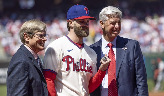 Philadelphia Phillies&#x27; Bryce Harper, center, displays his championship ring with Phillies President Dave Dombrowski, right, and CEO John Middleton during the National League ring ceremony before a baseball game against the Cincinnati Reds, Sunday, April 9, 2023, in Philadelphia. (AP Photo/Laurence Kesterson) **FILE**