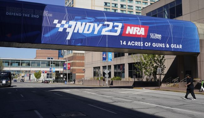 A pedestrian walks under a sign advertising the NRA Convention, Thursday, April 13, 2023, in Indianapolis. The convention starts Friday, April 14 and end on Sunday, April 16. (AP Photo/Darron Cummings)