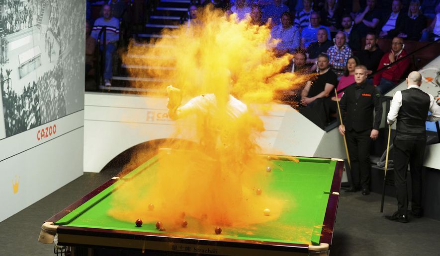 A 'Just Stop Oil' protester jumps on the table and throws orange powder during the match between Robert Milkins against Joe Perry as part of day three of the World Snooker Championship at the Crucible Theatre, Sheffield, Britain, Monday, April 17, 2023. (Mike Egerton/PA via AP)
