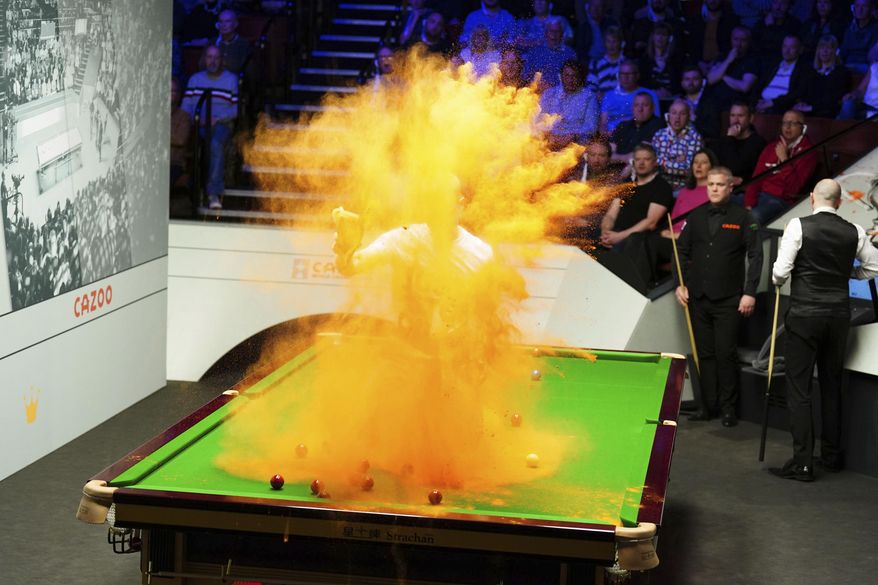A 'Just Stop Oil' protester jumps on the table and throws orange powder during the match between Robert Milkins against Joe Perry as part of day three of the World Snooker Championship at the Crucible Theatre, Sheffield, Britain, Monday, April 17, 2023. (Mike Egerton/PA via AP)
