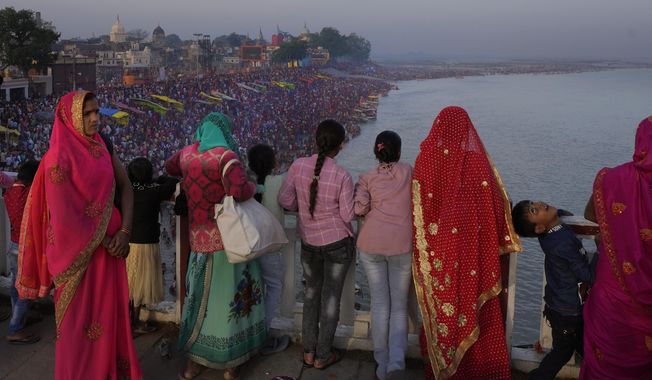 Families watch from a bridge as thousands of people enter the holy River Saryu in Ayodhya, India, Thursday, March 30, 2023. The United Nations says India will be the world’s most populous country by the end of this month, eclipsing an aging China. (AP Photo/Manish Swarup)