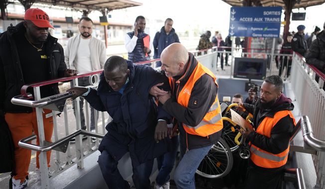 A disable man is helped climbing the stair to access the platform Wednesday, April 26, 2023 at the Melun train station, outside Paris. An influential disabled rights group in France is boycotting a conference on disability Wednesday with French President Emmanuel Macron, amid frustration at dismal accessibility for people in wheelchairs and with other mobility challenges -- and years of unmet promises to make things better ahead of the Paris 2024 Olympic and Paralympic Games. (AP Photo/Christophe Ena)
