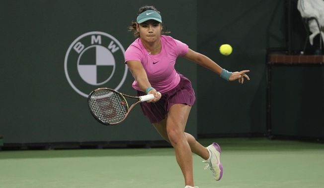 Emma Raducanu, of Britain, returns a shot to Iga Swiatek, of Poland, at the BNP Paribas Open tennis tournament Tuesday, March 14, 2023, in Indian Wells, Calif. Raducanu will miss the French Open and Wimbledon after announcing that minor surgery on both hands and an ankle will sideline her for “the next few months.” The 2021 U.S. Open champion has struggled with injuries in recent months and pulled out of the Madrid Open because of a hand problem. (AP Photo/Mark J. Terrill, File)
