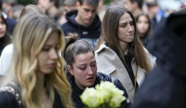 People bring flowers for the victims in front of the Vladimir Ribnikar school in Belgrade, Serbia, Thursday, May 4, 2023. A 13-year-old who opened fire Wednesday at his school in Serbia&#x27;s capital killed eight fellow students and a guard before calling the police and being arrested. Six children and a teacher were also hospitalized. (AP Photo/Darko Vojinovic)