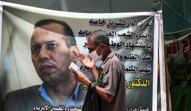 A protester prays by a poster showing Hisham al-Hashimi, on July 12, 2020, an Iraqi analyst who was a leading expert on the Islamic State and other armed groups and was shot dead in Baghdad. An Iraqi court on Sunday, May 7, 2023, issued a death sentence against the alleged killer of prominent Iraqi security analyst Hisham al-Hashimi, nearly three years after his assassination. (AP Photo/Khalid Mohammed, File)