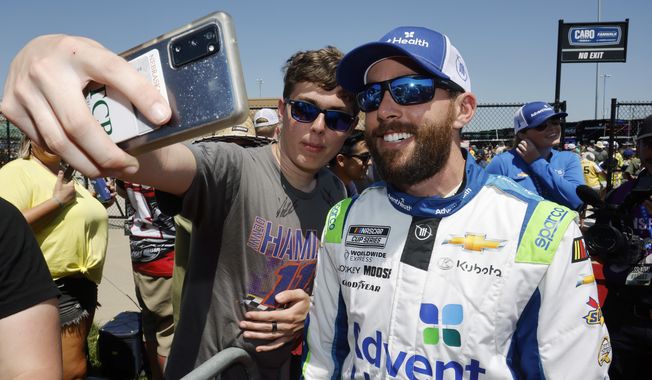 A fan, left, takes a photo with Ross Chastain, right, before a NASCAR Cup Series auto race at Kansas Speedway in Kansas City, Kan., Sunday, May 7, 2023. (AP Photo/Colin E. Braley)