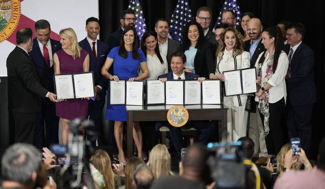 Florida Governor Ron DeSantis, center, and other elected, state, and local officials pose with a group of education-related bills after DeSantis signed them into law at a news conference in Miami, Tuesday, May 9, 2023. (AP Photo/Rebecca Blackwell)