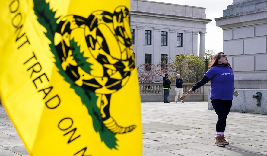Ryan Olski yells and bangs on a pot in front of a Gadsden flag while a group protests before the signing of firearms regulation bills by Washington Gov. Jay Inslee, Tuesday, April 25, 2023, outside the Capitol in Olympia, Wash. (AP Photo/Lindsey Wasson)