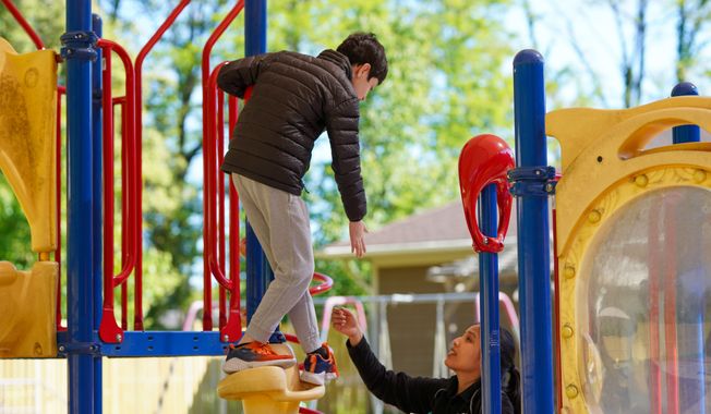 An intellectually disabled boy plays with a staffer on the adaptive playground at Jill’s House, an evangelical Christian ministry in Vienna, Virginia, on Saturday, May 6, 2023. (All Pro Reels, Olivia Evans, Special to The Washington Times)