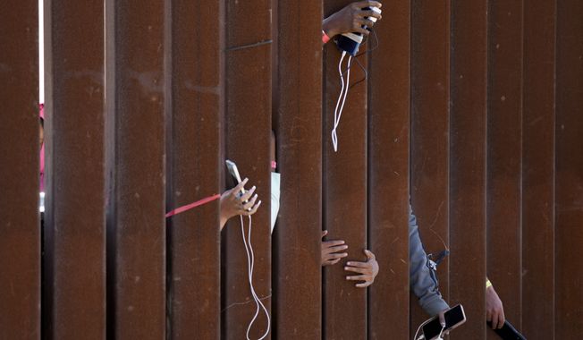 Migrants waiting to apply for asylum between two border walls hold out phones in hopes of getting a charge Thursday, May 11, 2023, in San Diego. Pandemic-related U.S. asylum restrictions, known as Title 42, are to expire May 11. (AP Photo/Gregory Bull)