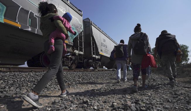 Migrants walk alongside a train going past as they wait to board a freight train heading north, one that stops long enough so they can hop on, in Huehuetoca, Mexico, Friday, May 12, 2023, the day after U.S. pandemic-related asylum restrictions called Title 42 were lifted. (AP Photo/Marco Ugarte)