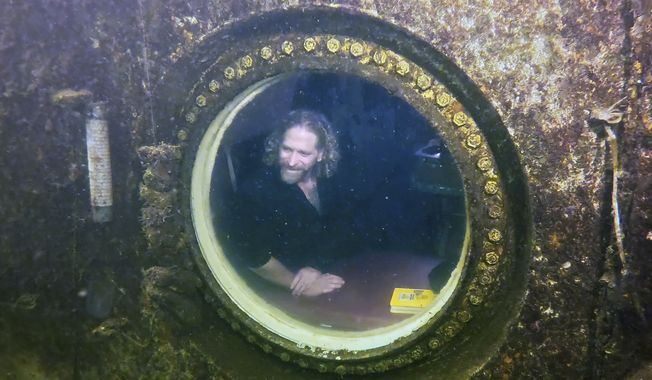 In this photo provided by the Florida Keys News Bureau, diving explorer and medical researcher Joseph Dituri peers out of a large porthole, Saturday, May 13, 2023, at Jules&#x27; Undersea Lodge positioned at the bottom of a 30-foot-deep lagoon in Key Largo, Fla. On Saturday, Dituri broke a record for the longest time living underwater at ambient pressure, his 74th day of a planned 100-day mission living submerged in the Florida Keys. (Frazier Nivens/Florida Keys News Bureau via AP)