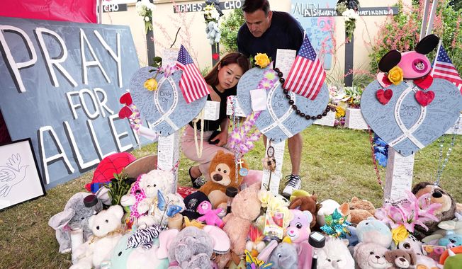 Angela Munoz, leaves a message on a cross with the name, Cindy Cho, as her husband Rick, looks on at a makeshift memorial, Wednesday, May 10, 2023, in Allen, Texas, by the mall where several people were killed. The cross for Cho stands by those of her family, Kyu, and James. (AP Photo/Tony Gutierrez)