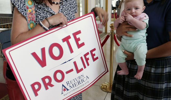 An anti-abortion supporter from Moore County holds a sign next to a 3-month-old baby as they wait to enter the Senate gallery, Tuesday, May 16, 2023, in Raleigh, N.C., as state legislators debate on whether to override Democratic Gov. Roy Cooper&#x27;s veto of a bill that would change the state&#x27;s ban on nearly all abortions from those after 20 weeks of pregnancy to those after 12 weeks of pregnancy. Both the Senate and House had to complete successful override votes for the measure to be enacted into law. (AP Photo/Chris Seward)