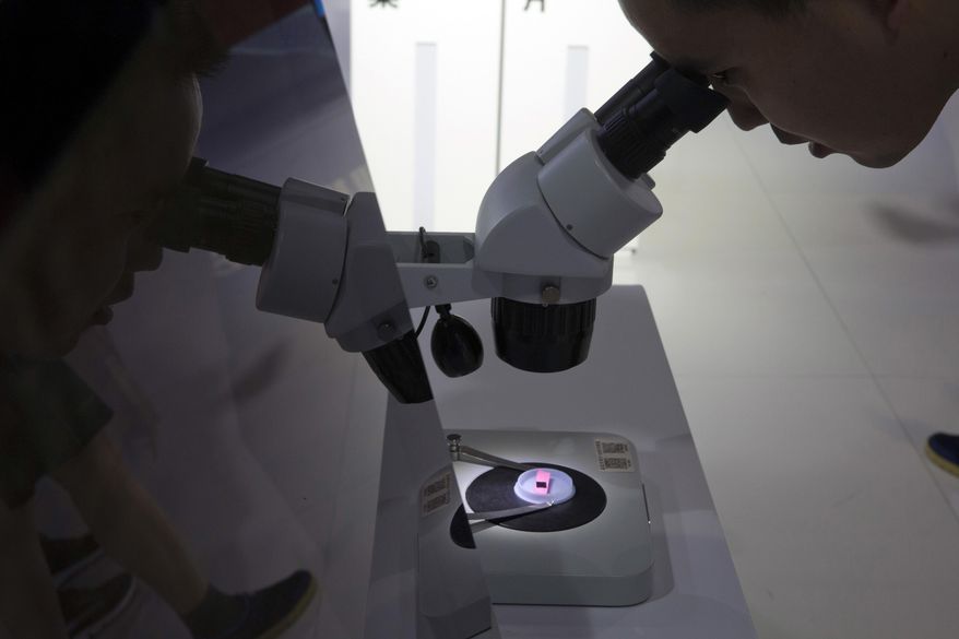 A visitor to the 21st China Beijing International High-tech Expo looks at a computer chip through the microscope displayed by the state-controlled Tsinghua Unigroup project which has emerged as a national champion for Beijing's semiconductor ambitions in Beijing, on May 17, 2018. Britain's government unveiled its long-awaited semiconductor strategy Friday, May 19, 2023, catching up with similar efforts by Western allies seeking to reduce reliance on Asian production of the computer chips that are essential to modern life. (AP Photo/Ng Han Guan, File)