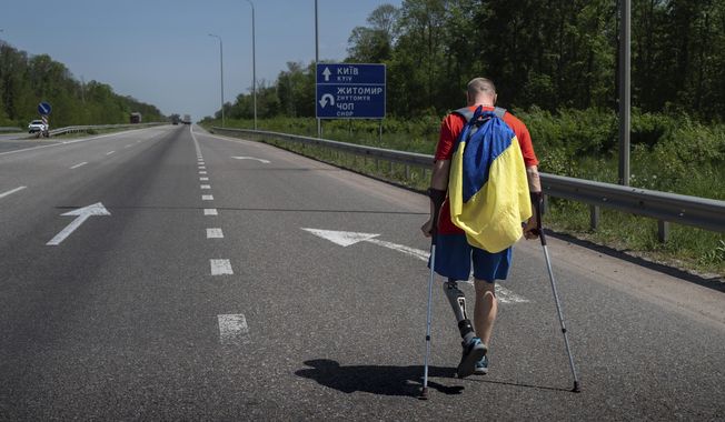 Ukrainian war veteran Oleksandr Shvetsov carries a Ukrainian flag as he walks along a highway towards Kyiv from Zhytomyr to meet his friend Serhii Khrapko ahead of their 120-kilometer (75 mile) walk to raise money for medical equipment in honor of their comrades wounded in Russia&#x27;s war against their homeland in Stavyshche village, Zhytomyr region, Ukraine, on Thursday, May 18, 2023. They raised 3.1 million hryvnias ($84,000), short just the 500,000 hryvnias ($14,000) needed to purchase a new gastroscope for Ukraine&#x27;s National Military Medical Clinical Center. (AP Photo/Roman Hrytsyna)