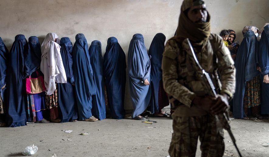 A Taliban fighter stands guard as women wait to receive food rations distributed by a humanitarian aid group, in Kabul, Afghanistan, Tuesday, May 23, 2023. (AP Photo/Ebrahim Noroozi)