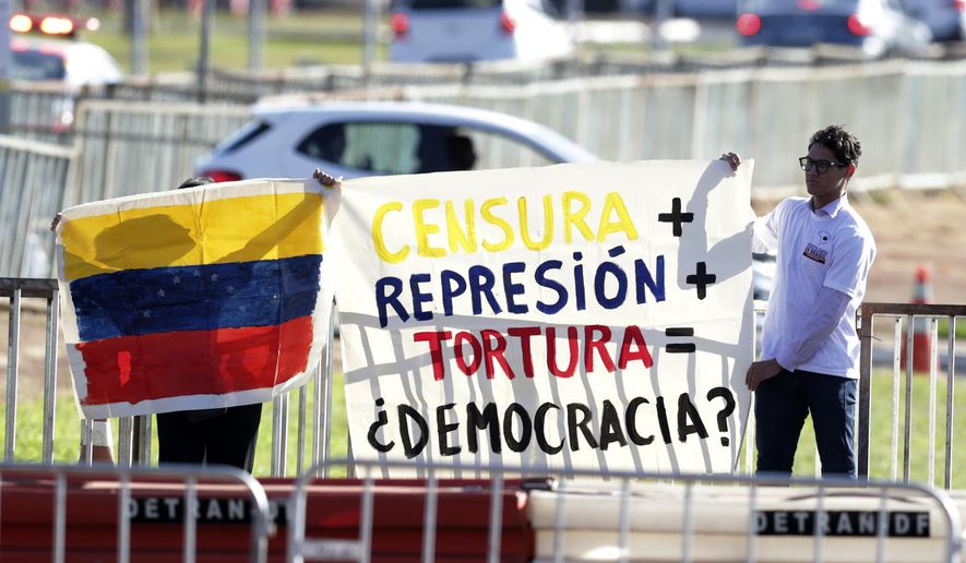 People hold a Venezuelan flag and sign that reads "Censorship, plus repression, plus torture, equals democracy?" outside Itamaraty palace where regional leaders are attending the South American Summit in Brasilia, Brazil, Tuesday, May 30, 2023. South America’s leaders are gathering as part of President Luiz Inácio Lula da Silva’s attempt to reinvigorate regional integration efforts. (AP Photo/Gustavo Moreno)
