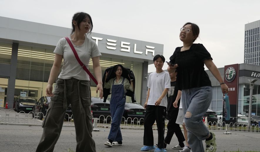 Young Chinese walk past a Tesla showroom in Beijing, Tuesday, May 30, 2023. China’s foreign minister met Tesla Ltd. CEO Elon Musk on Tuesday and said strained U.S.-Chinese relations require “mutual respect,” while delivering a message of reassurance that foreign companies are welcome. (AP Photo/Ng Han Guan) ** FILE **