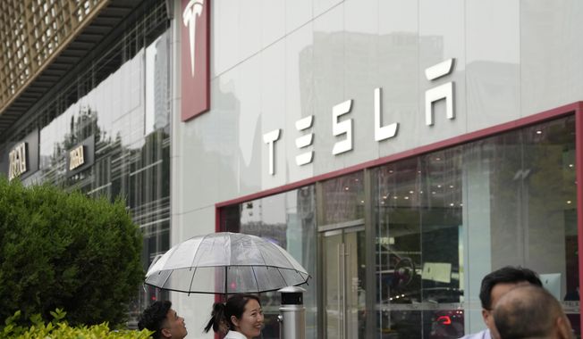 Workers chat under an umbrella outside the Tesla showroom in Beijing, Tuesday, May 30, 2023. China鈥檚 foreign minister met Tesla Ltd. CEO Elon Musk on Tuesday and said strained U.S.-Chinese relations require 鈥渕utual respect,鈥� while delivering a message of reassurance that foreign companies are welcome. (AP Photo/Ng Han Guan)