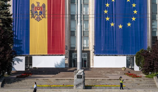 A woman runs past the government building, decorated with European Union and Moldovan flags in Chisinau, Moldova, Wednesday, May 31, 2023. Moldova will host the Meeting of the European Political Community on June 1, 2023. Preparations for a major summit of European leaders were still underway in Moldova on Wednesday, a sign of the Eastern European country’s ambitions to draw closer to the West and break with its Russian-dominated past amid the war in neighboring Ukraine. (AP Photo/Vadim Ghirda)