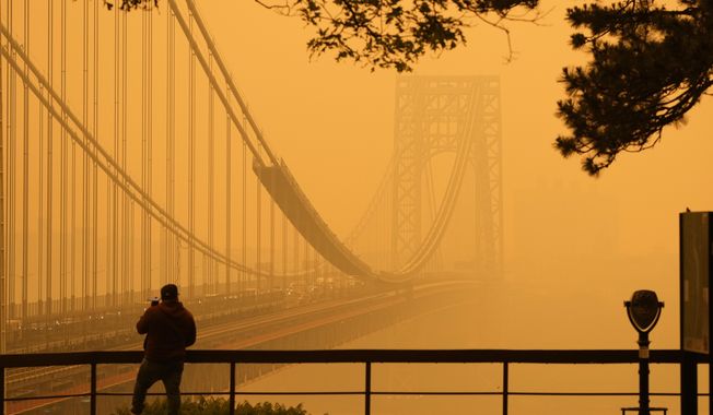 A Man talks on his phone as he looks through the haze at the George Washington Bridge from Fort Lee, N.J., Wednesday, June 7, 2023. Intense Canadian wildfires are blanketing the northeastern U.S. in a dystopian haze, turning the air acrid, the sky yellowish gray and prompting warnings for vulnerable populations to stay inside. (AP Photo/Seth Wenig)