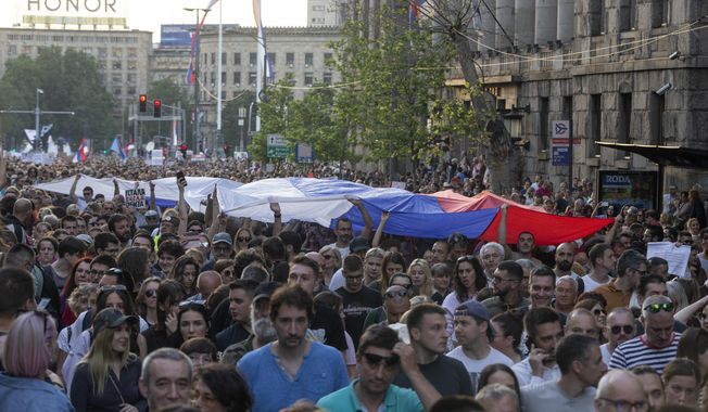People hoist a Serbian flag as they walk down a street during an anti-government protest in Belgrade, Serbia, Saturday, June 3, 2023. Tens of thousands of people rallied in Serbia&#x27;s capital on Saturday in protest of the government&#x27;s handling of a crisis after two mass shootings in the Balkan country. (AP Photo/Marko Drobnjakovic)