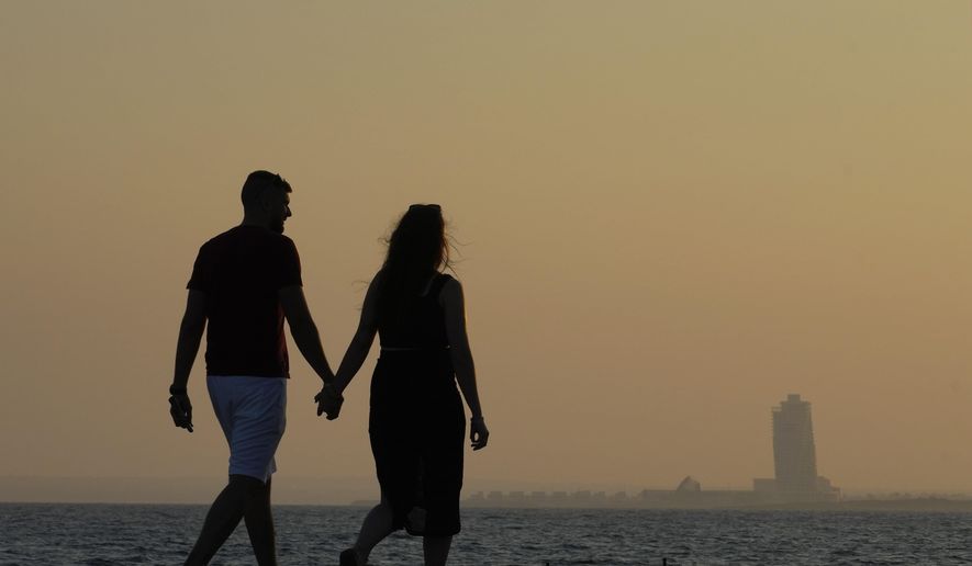A couple walk by the sea as in the background is seen an apartments tower of a new construction of "Ayia Napa Marina", during sunset in the resort of Ayia Napa in the eastern Mediterranean island of Cyprus, on Tuesday, June 6, 2023. When the U.S. and U.K. in April included a handful of Cypriot nationals and Cyprus-registered companies as part of another global crackdown on 'enablers' helping Russian oligarchs skirt sanctions, the perception that the island nation somehow remains Moscow's financial lackey again loomed large. (AP Photo/Petros Karadjias)