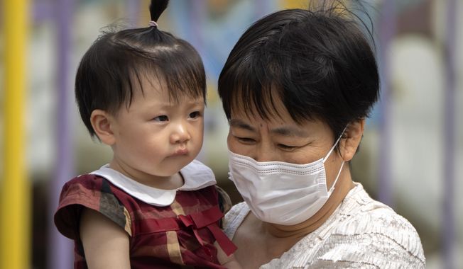 FILE - A woman wearing a face mask carries a child as they walk at a public park in Beijing, on June 1, 2023. China reported Thursday, July 6, 2023 that 239 people died from COVID-19 in June in a significant uptick months after it lifted most containment measures. (AP Photo/Mark Schiefelbein, File)