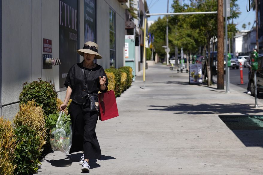 A woman walks with a bag of groceries under the midday sun, Tuesday, July 11, 2023, in Los Angeles. Southern California is expecting high temperatures between 100 to 110 degrees Fahrenheit later this week according to the National Weather Service. (AP Photo/Ryan Sun)