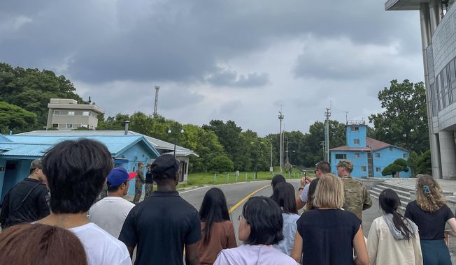 A group of tourists stands near a border station at Panmunjom in the Demilitarized Zone in Paju, South Korea, Tuesday, July 18, 2023. Not long after this photo was taken, Travis King, a U.S. soldier, pictured with dark blue shirt and dark cap, fourth left, bolted across the border and became the first known American detained in the North in nearly five years. (AP Photo/Sarah Jane Leslie)